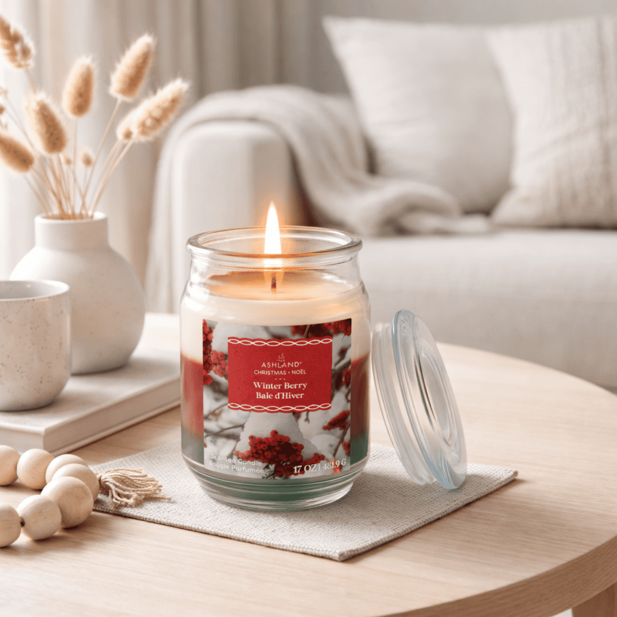 Candle with a decorative label 'Winter Berry' on a table in a cozy living room setting