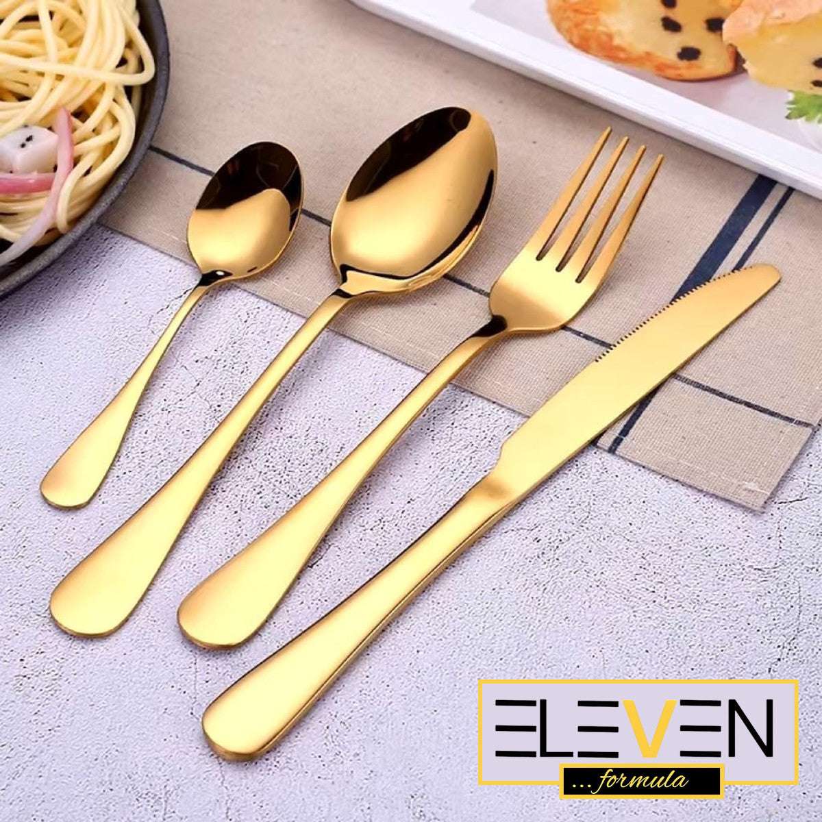 Close-up of Eleven Formula 16 Piece Gold Stainless Steel Silverware Set beside plated food, featuring brand logo and polished finish.
