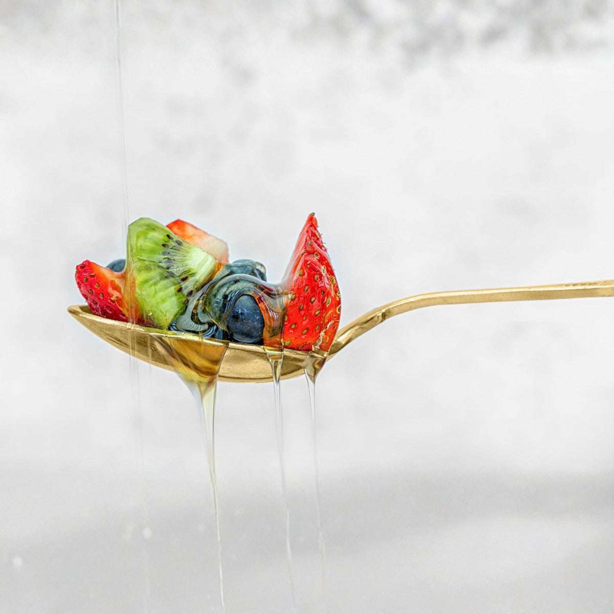 Gold stainless steel spoon from the Eleven Formula set holding fresh fruit and honey, showcasing durability and elegance in use.