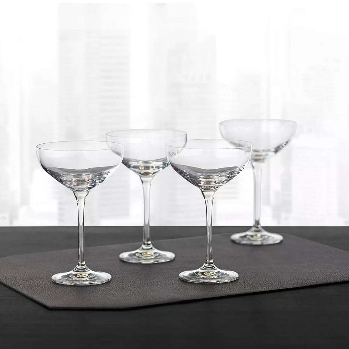 Set of four Hotel Collection Champagne Coupe Glasses 9.7 oz displayed on a dark mat, perfect for upscale home bar or entertaining settings.