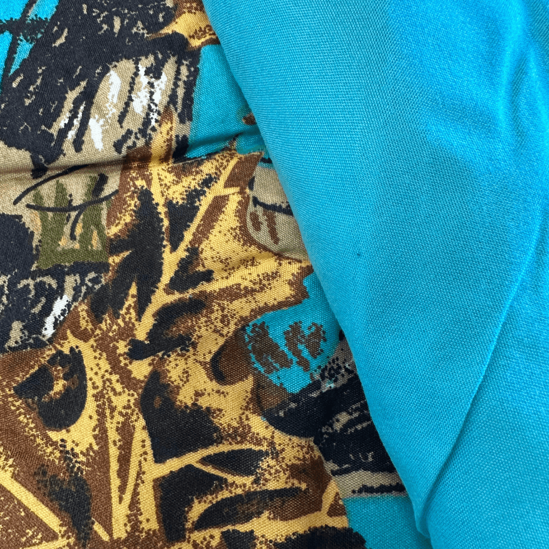 Close-up of The Woods Seabreeze Twin Sheet Set fabric showing detailed nature print and solid turquoise material side by side.