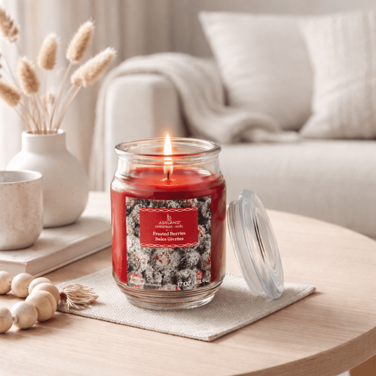 Red candle labeled 'Frosted Berries' on a table in a cozy living room setting