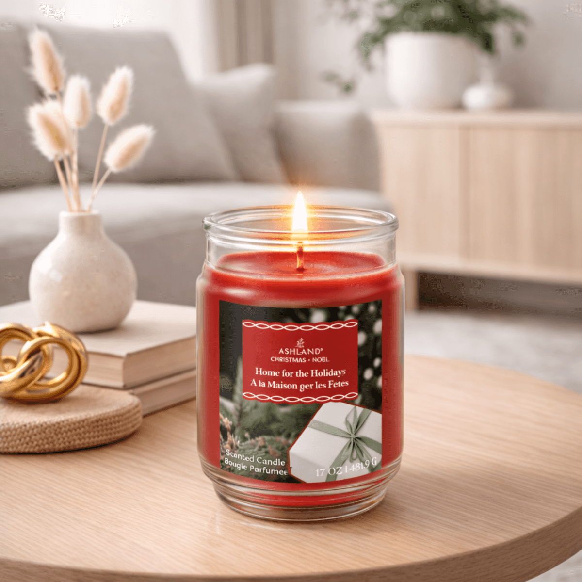 Lit holiday scented candle in glass jar on cozy living room table