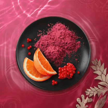 Close-up of pink and red powder with orange slices and berries on a black plate