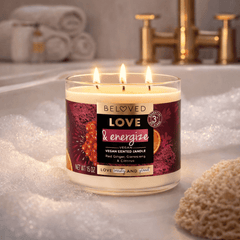 Lit candle on a bathroom counter with bubbles, towels, and gold fixtures