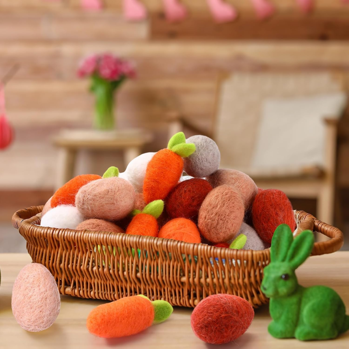 Wicker basket filled with felted wool carrots and eggs on a wooden surface.