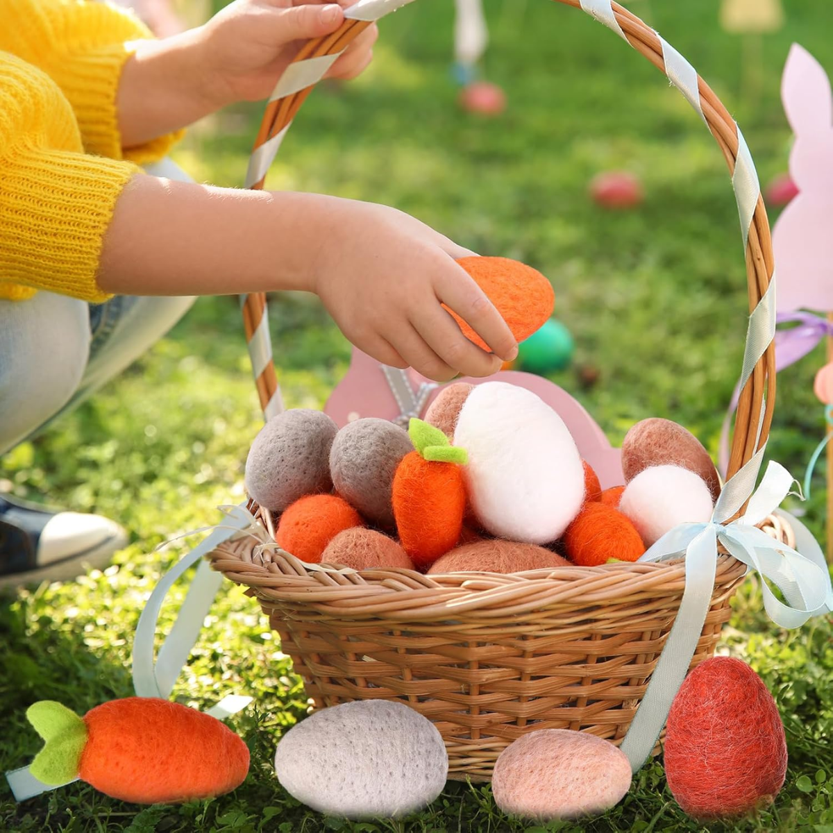 Wicker basket filled with felt Easter eggs and carrots on grass