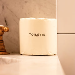 Light cream toilet paper roll Toilette NYC with TOILETTE NYC label on wrapped package for bathroom countertop display