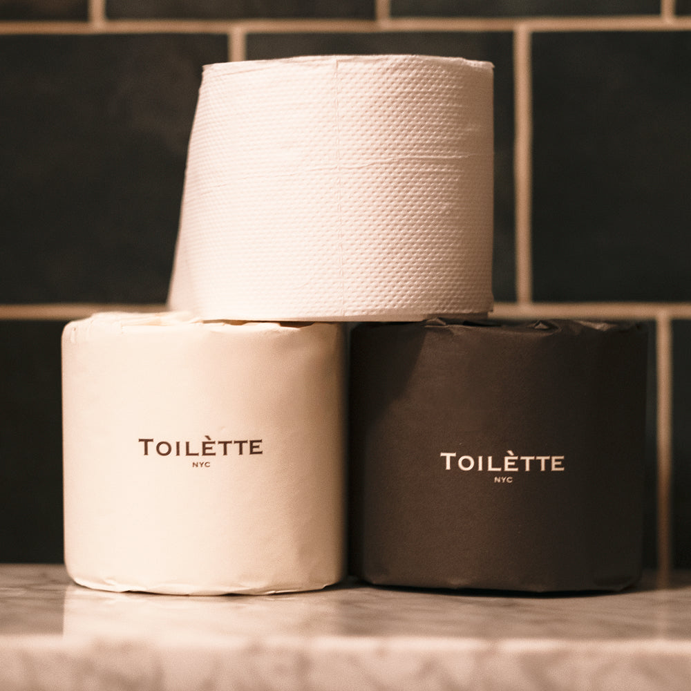 Toilètte toilet paper rolls in mixed light and dark paper, stacked rolls with Toilètte NYC branding on tabletop, set of two