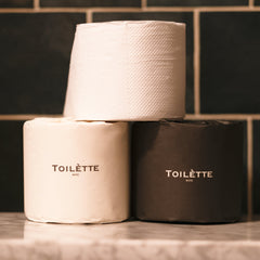 Toilètte toilet paper rolls in mixed light and dark paper, stacked rolls with Toilètte NYC branding on tabletop, set of two