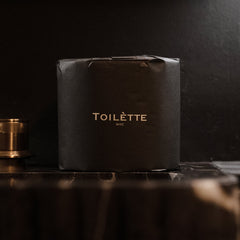 Dark toilet paper rolls in a square black package by Toilètte, with Toilètte NYC logo printed in gold at center panel