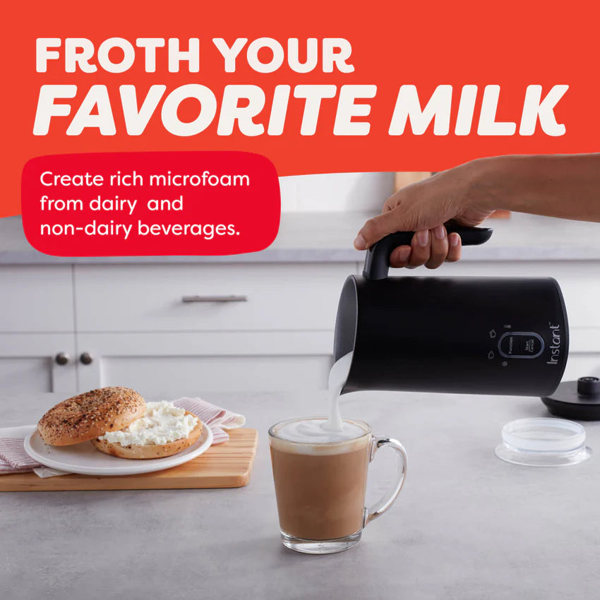 Person using a milk frother to create foam in a glass of coffee on a kitchen counter.