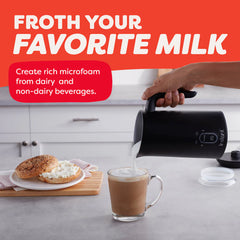 Person using a milk frother to create foam in a glass of coffee on a kitchen counter.