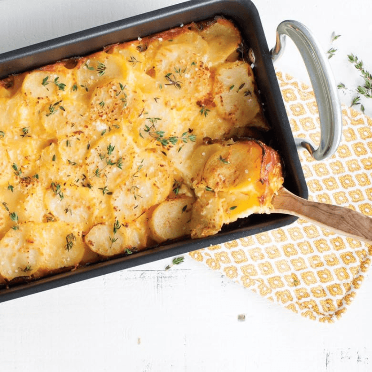 Cheesy potato casserole in a Nordic Ware baking dish with a wooden spoon on a patterned napkin.