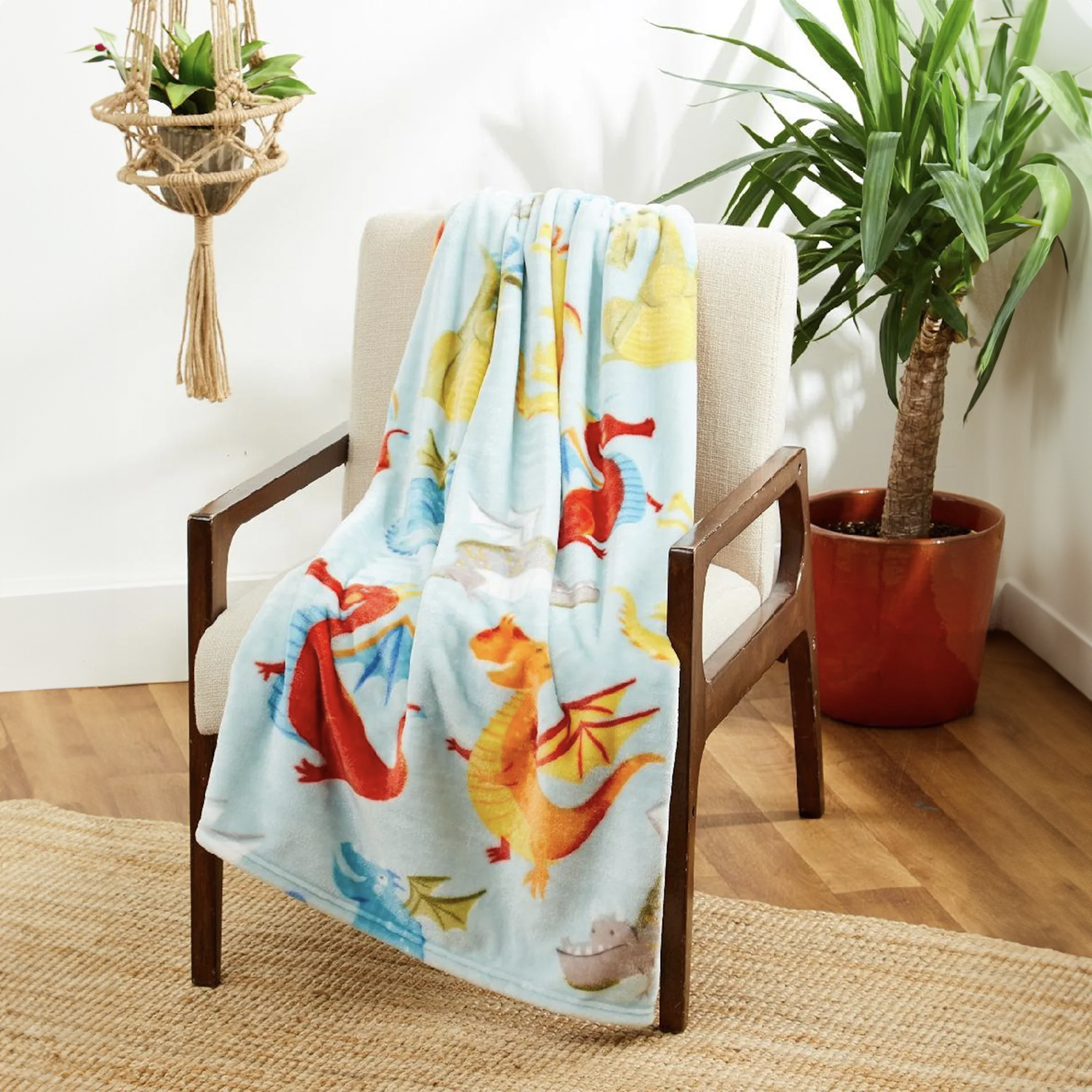 Colorful dragon-themed blanket by Regal Comfort draped over a chair in a room with plants and wooden floor.