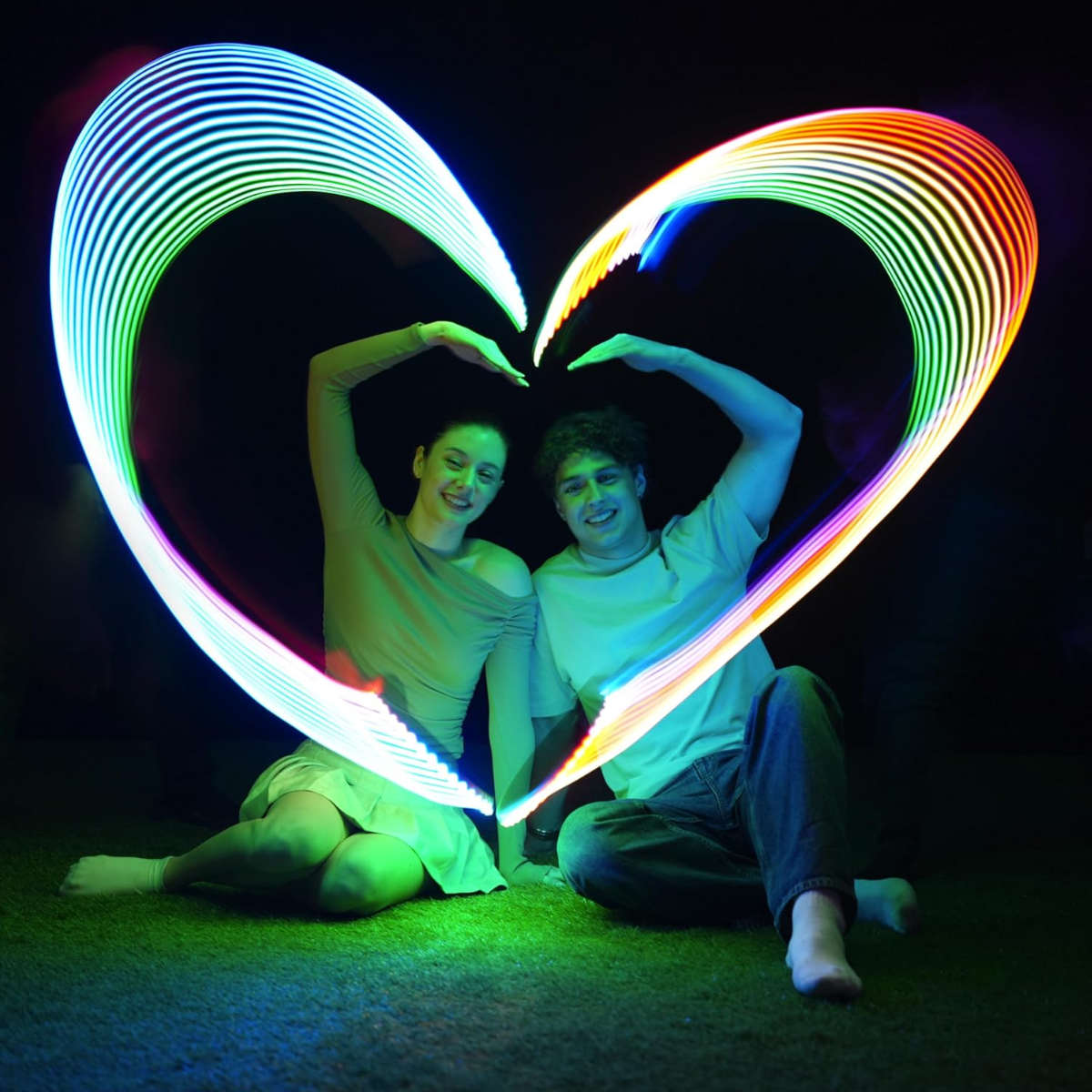 Two people holding glowing heart-shaped lights against a dark background
