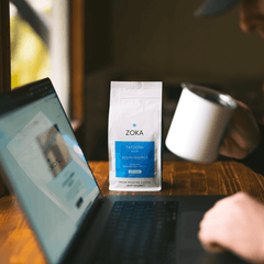 Person using laptop with Zoka Tatoosh coffee bag on wooden table